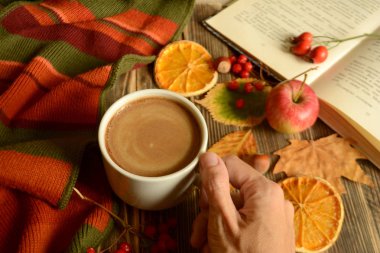 Sonbahar kompozisyon kahve Kupası el, kitap, renkli atkı, yaprakları, elma, portakal ahşap arka plan sonbahar kavram rahat bir ev üzerinde kurutulmuş