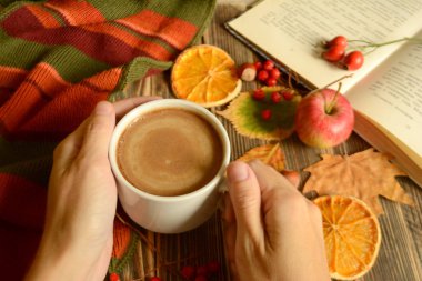 Sonbahar kompozisyon kahve Kupası el, kitap, renkli atkı, yaprakları, elma, portakal ahşap arka plan sonbahar kavram rahat bir ev üzerinde kurutulmuş