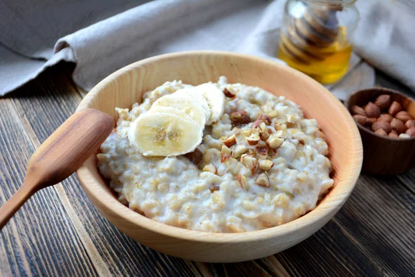 Oatmeal porridge with bananas, nuts and honey in a wooden bowl