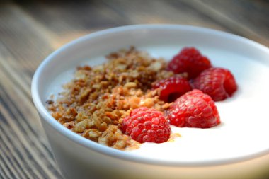Ahşap arka plan sağlıklı gıda konsepti üzerinde bir kase granola ve taze ahududu ile lezzetli yoğurt 