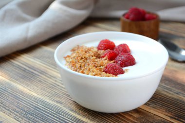 Ahşap arka plan sağlıklı gıda konsepti üzerinde bir kase granola ve taze ahududu ile lezzetli yoğurt 