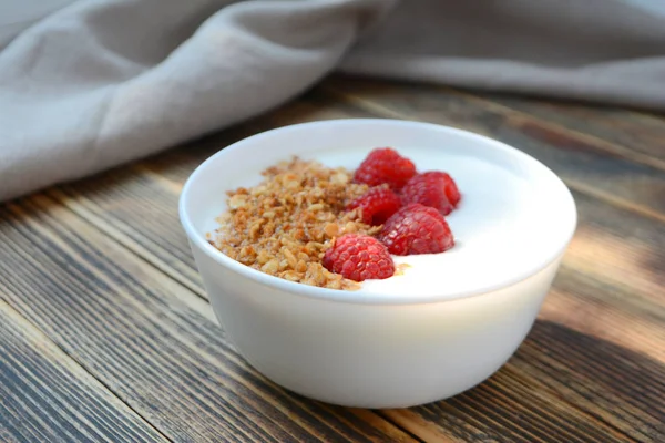 Ahşap arka plan sağlıklı gıda konsepti üzerinde bir kase granola ve taze ahududu ile lezzetli yoğurt 
