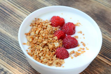 Ahşap arka plan sağlıklı gıda konsepti üzerinde bir kase granola ve taze ahududu ile lezzetli yoğurt 