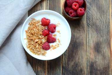 Ahşap bir arka planda bir kase granola ve taze ahududu ile lezzetli yoğurt sağlıklı gıda kavramı üst görünüm