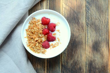 Ahşap bir arka planda bir kase granola ve taze ahududu ile lezzetli yoğurt sağlıklı gıda kavramı üst görünüm