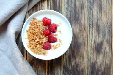 Ahşap bir arka planda bir kase granola ve taze ahududu ile lezzetli yoğurt sağlıklı gıda kavramı üst görünüm