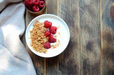 Ahşap bir arka planda bir kase granola ve taze ahududu ile lezzetli yoğurt sağlıklı gıda kavramı üst görünüm