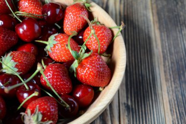Kahverengi ahşap bir kasede çilek ve kiraz. Taze organik yaz meyveleri