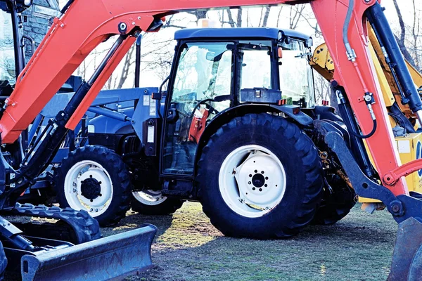 Başka bir makinenin kırmızı kolu tarafından çerçevelenmiş mavi bir traktör..