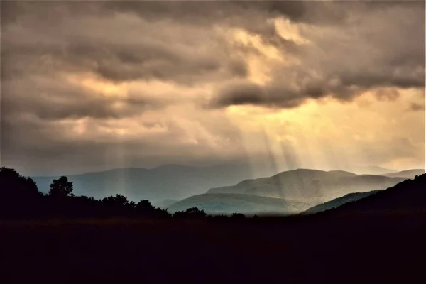 Çoklu güneş ışınları dağların üzerindeki fırtına bulutlarını dağıtıyor.