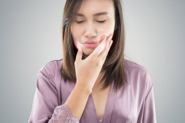 Temporomandibular Joint and Muscle Disorder: TMD, Suffering from toothache. Beautiful young woman suffering from toothache while standing against grey background clipart