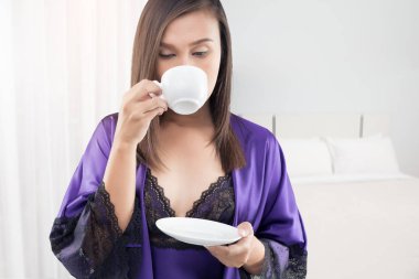 İpek gecelik ve yatak odası sabah, sabah seksi kız, sıcak kahve bir fincan beyaz fincan çay bir menekşe gecelik yatakta ile mor dantel elbise kadında.