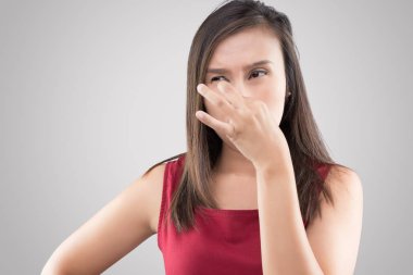 Asian woman in red shirt holding her nose because of a bad smell on gray background. clipart