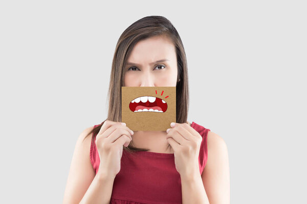 Азиатка в красной рубашке держит коричневую бумагу со сломанным карикатурным рисунком рта на сером фоне, гнилой зуб, концепция с медицинскими деснами и зубами