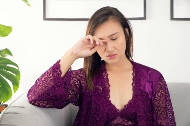 Kaşındıran bir göz kapağı, gecelikli Asyalı kadınlar ve mor saten bornoz giyip gözlerini ovuşturan gece oturma odasındaki gri koltukta oturan ipek gecelikli bir kız sağ göz kapağını kaşındırdığı için kaşınıyor.