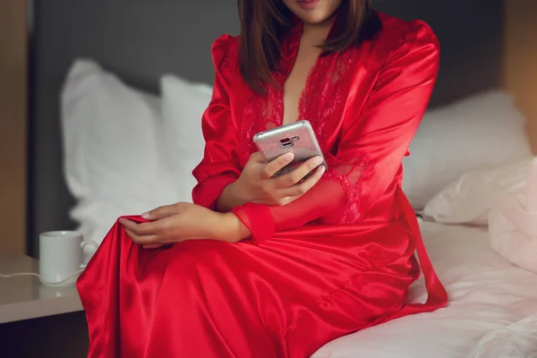 Asiatico Donna Rosso Raso Accappatoi Utilizzando Cellulare Mentre Seduta Letto — Foto Stock