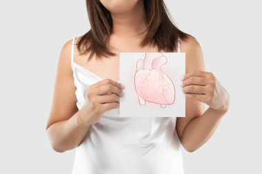 A woman in the white dress holding a light gray paper with the heart picture of his chest on a gray background, Coronary artery disease, The concept of heart disease and medical treatmen clipart