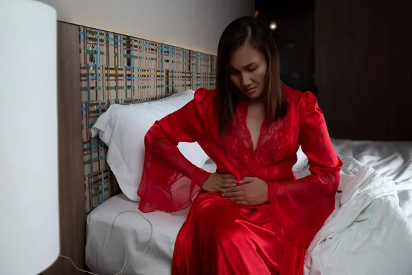 Have a pain under right waist. A woman in satin nightgown and red robes in pain holding his stomach and rib pain on right side in the bedroom at night.