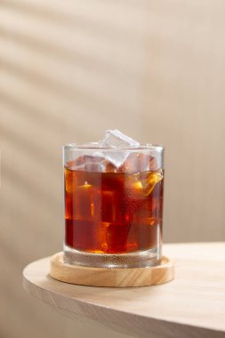 Bir bardak buzlu Americano kahvesi, ahşap bir masada kristal buz küpleri, kahve severler için mükemmel, serinletici bir soğuk bira anı arıyor..