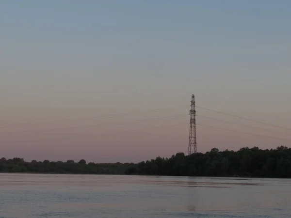 Αυγή ακτή γκρι ουρανό ροζ φως σε ένα ποτάμι της πόλης με ένα τοπίο με ένα μαύρο πύργο. — Φωτογραφία Αρχείου