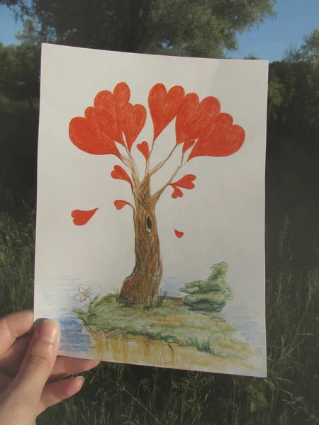 Een hand houdt een tekening van een fantastische boom met rode harten in het licht van de rijzende zon. — Stockfoto