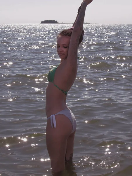 Una ragazza abbronzata con dreadlocks viola, tatuaggi e un piercing si erge in acqua contro l'orizzonte del mare con yacht . — Foto Stock