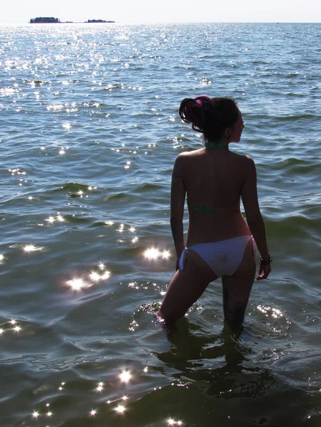 A tanned girl with purple dreadlocks, tattoos and a piercing stands in the water against of the sea surface. — Stock Photo, Image