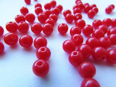 İğne işi için parlak kırmızı yuvarlak boncuklar rastgele beyaz bir arka plan üzerinde dağınık.