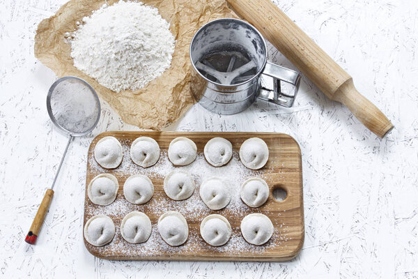 Процесс приготовления домашних пельменей. Сырые домашние пельмени на деревянной доске. Формовочные пельмени.