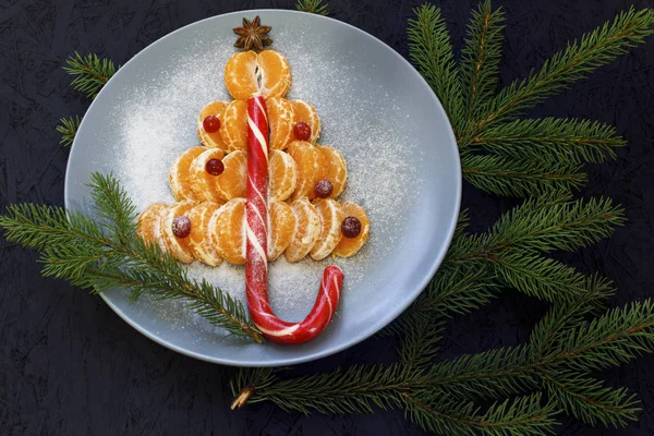 Mandalina dilimleri ile bir plaka üzerinde bir Noel ağacı şeklinde ortaya koydu. Siyah arka plan ve çam dalları. Yukarıdan görüntüleyin. Yeni yıl ve Noel.