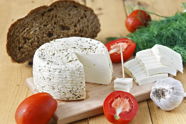 White cheese, bread, tomatoes and garlic on a wooden background.