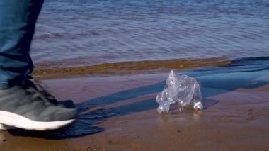 Plastikten deniz kıyısını temizlemek. Yazın kumlu bir sahilde plastik çöp toplayan bir adamın yakın çekimi. Çevre kirliliği kavramı. İnsan pisliği. Yavaş çekim.