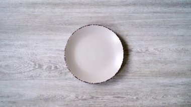Tasarım için açık ahşap zemin üzerinde boş beyaz bir plakanın yakın plan görüntüsü. Yemek tabağı ağacın arka planında. Videonun yavaş yaklaşımı kalıba, en üstteki görünüm.