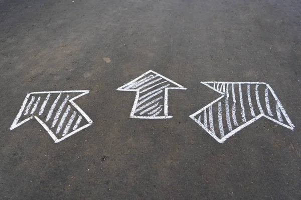 Three pointing arrows drawn in white chalk on the asphalt