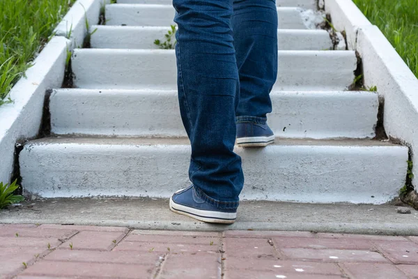 A man climbs the steps, legs in jeans and sneakers