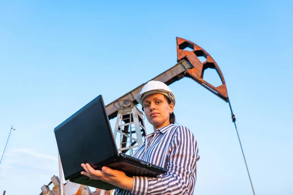 A female inspector with a laptop, in an oil field. Oil pumpers.