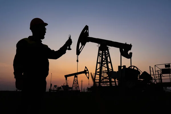 Silhouette of a chemical engineer taking a sample of crude oil against the background of oil pumps.