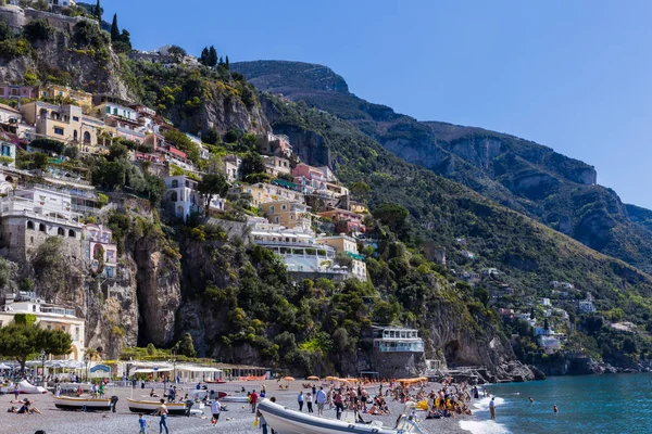 Positano, Costa Amalfitana, Itália - 9 de abril de 2017: muitas pessoas descansam na costa no fundo de montanhas com arquitetura tradicional italiana . — Fotografia de Stock