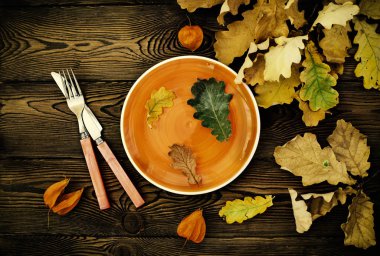 Şükran günü yemeği için sonbahar tablo ayarı. Boş tabak, çatal bıçak takımı, ahşap masa renkli yapraklarda. Sonbahar gıda kavramı
