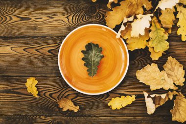 Şükran günü yemeği için sonbahar tablosu. Meşe yaprağı üstten görünüm bir turuncu plaka ve düşmüş renkli ahşap bir masaya bırakır. Sonbahar gıda kavramı