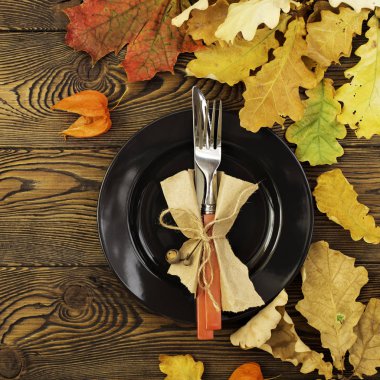 Şükran günü yemeği için sonbahar tablo ayarı. Boş tabak, çatal bıçak takımı, ahşap masa renkli yapraklarda. Sonbahar gıda kavramı