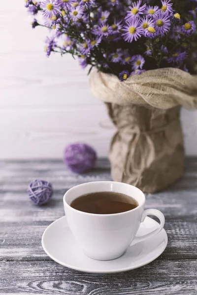 Романтический фон с чашкой чая, сиреневые цветы в вазе на сером деревянном столе — стоковое фото