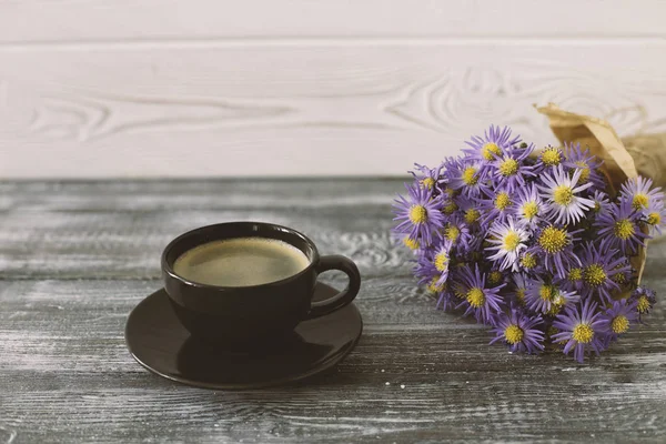 Романтический фон с чашкой кофе, букет фиолетовых цветов в ремесленной бумаге на сером деревянном столе — стоковое фото