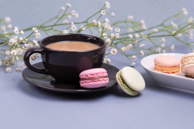Yakın çekim sabah siyah süt, pasta macaron ve çiçek mavi masada kahve fincan. Güzel tatlı