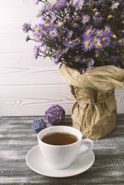Romantik bir arka plan, bir fincan çay, gri ahşap bir masada vazoda leylak çiçekleri..
