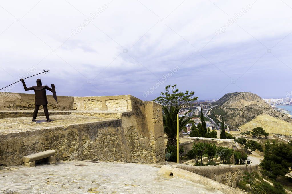 The figure of the Iron Knight with a spear on the tower of the fortress of Santa Barbara in Alicante. Spain. Panoramic view of the city, the harbor and the hills. Place to visit citizens and tourists.
