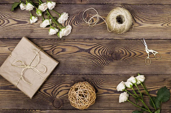 Regalo o scatola regalo avvolto in carta kraft e fiori, spago e forbici su sfondo di legno dall'alto. Stile piatto lay . — Foto Stock