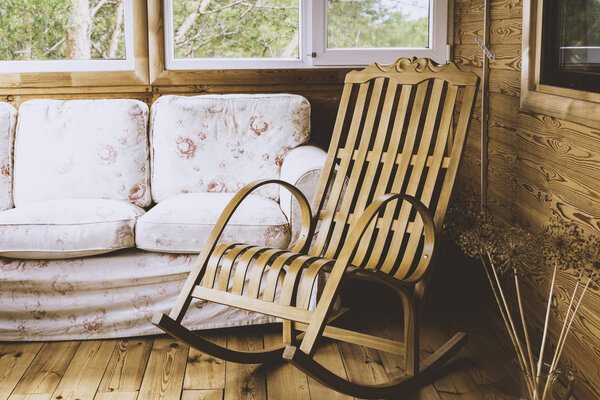 A wooden rocking chair and a sofa on the porch or terrace with a view of the forest. Tinted image
