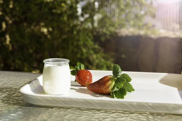Frische rote Erdbeeren und weißer Joghurt im Glas auf einem weißen Tablett auf einem Tisch im Garten oder auf der Terrasse an einem sonnigen Morgen — Stockfoto