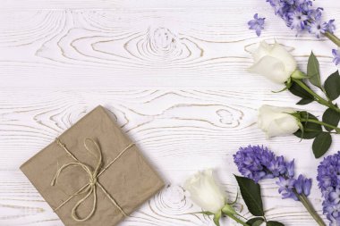 El işi kağıdına sarılı bir hediye kutusu ve mavi sümbül çiçekleri, beyaz bir masanın üstünde beyaz güller. Düz yatıyordu. Metin için alanı kopyala